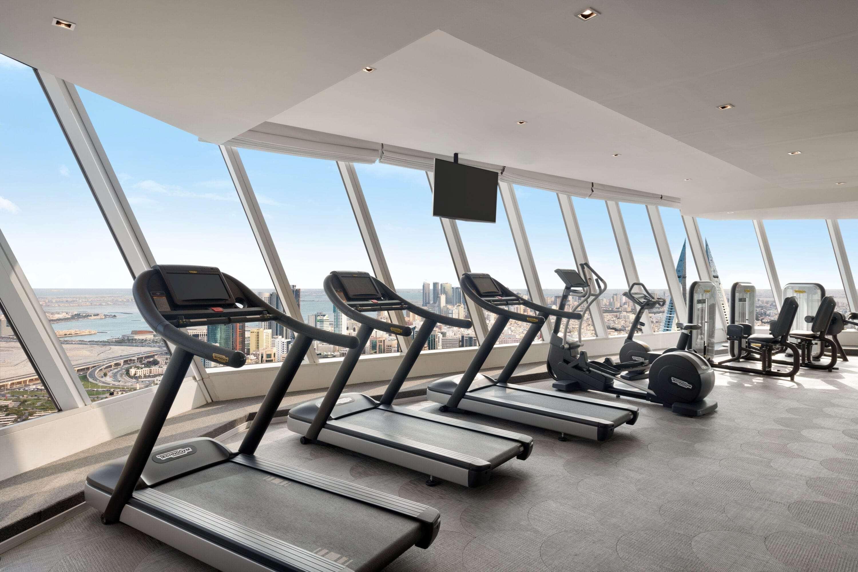 Wyndham Grand Manama Hotel Exterior photo The photo shows a modern gym area with large windows providing a panoramic view. There are several treadmills lined up, along with some other exercise equipment visible in the background. The space appears bright and well-lit, highlighting a clean an