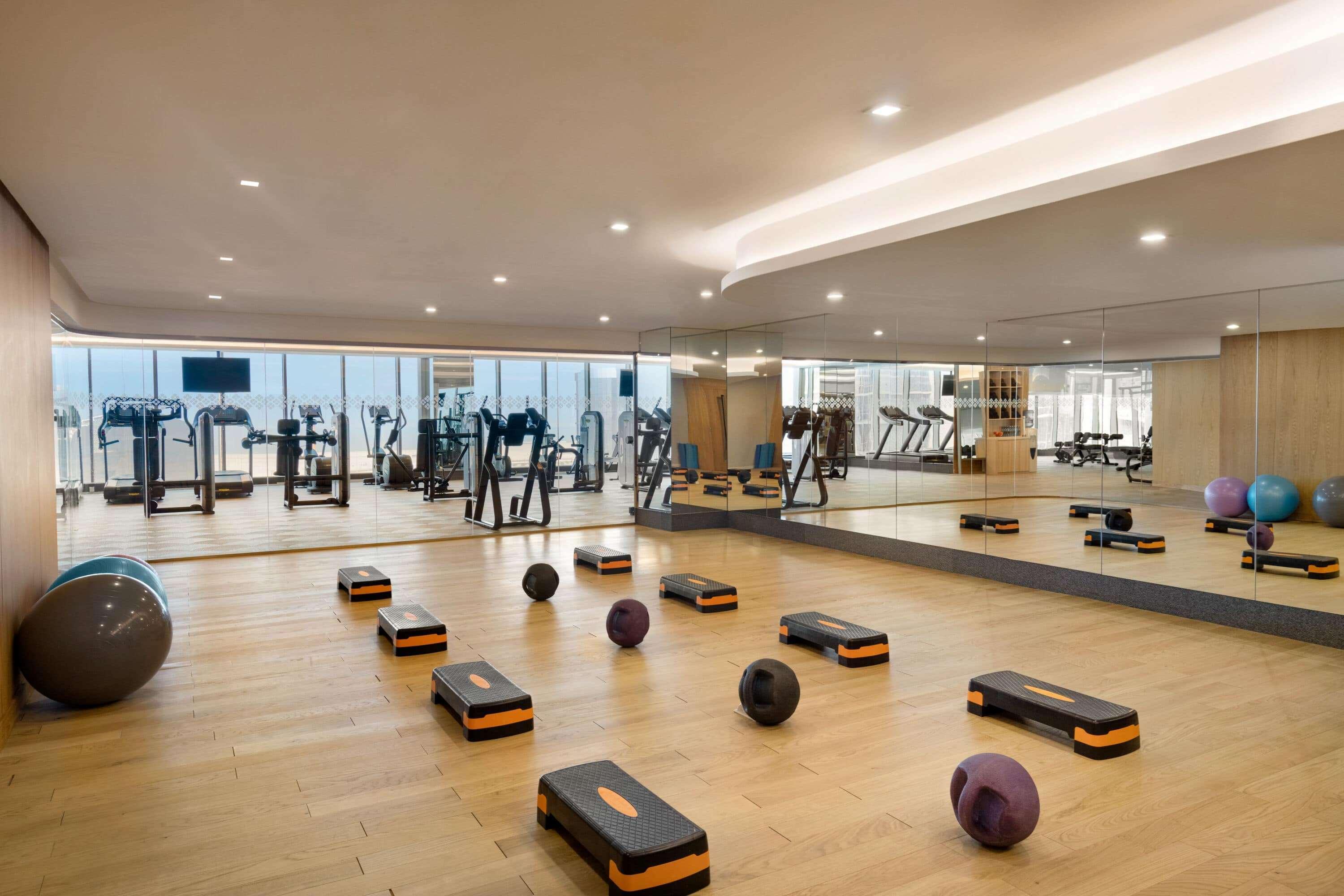 Wyndham Grand Manama Hotel Exterior photo The photo shows a modern gym or fitness studio. It features a spacious room with wooden flooring and bright overhead lighting. Along one side, there are various fitness equipment pieces, including treadmills and other exercise machines. The room is e