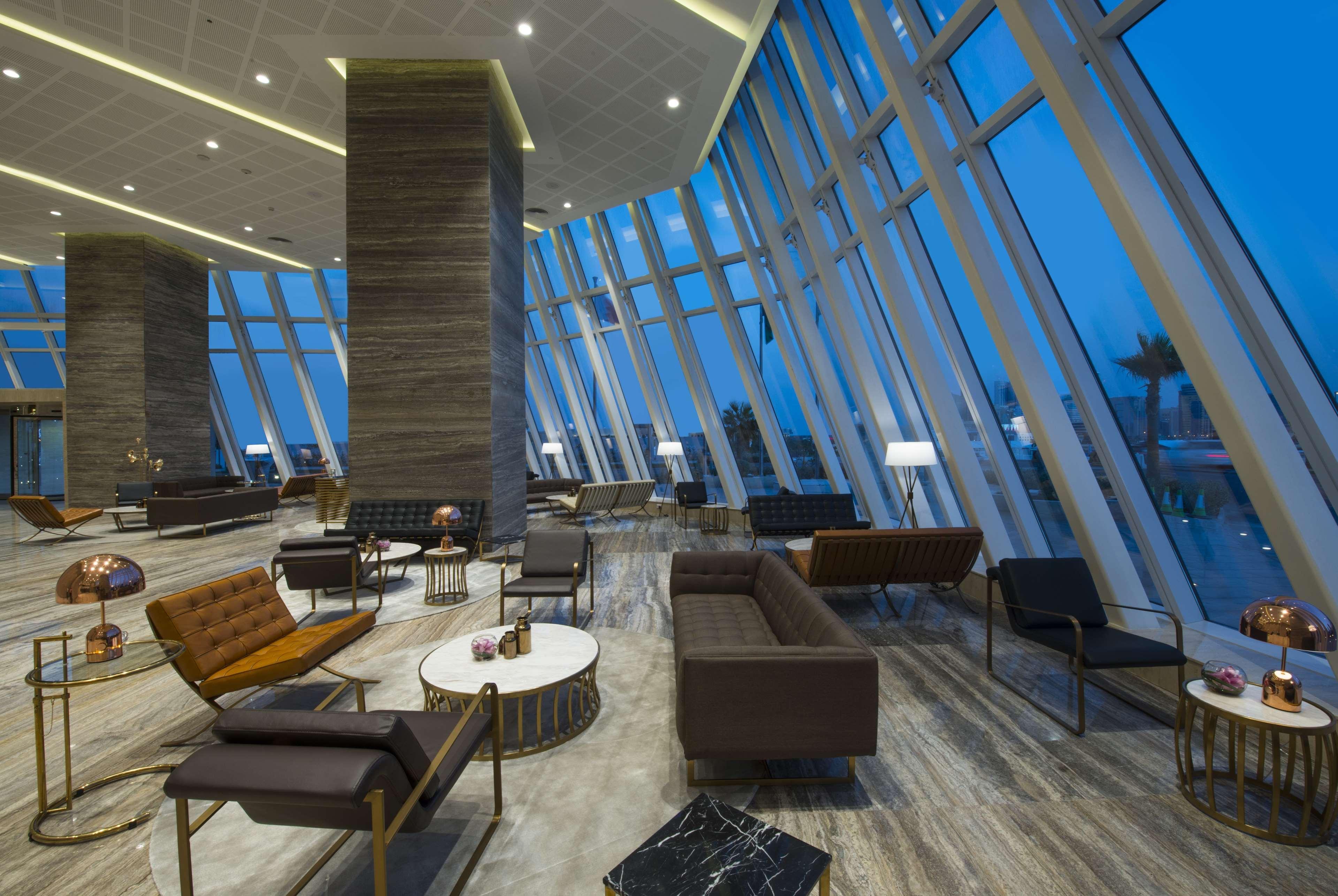 Wyndham Grand Manama Hotel Exterior photo The photo shows a modern lounge area with large windows allowing natural light to enter. The design features a mix of comfortable seating arrangements, including sofas and chairs, arranged around coffee tables. The interior includes sleek lines and a