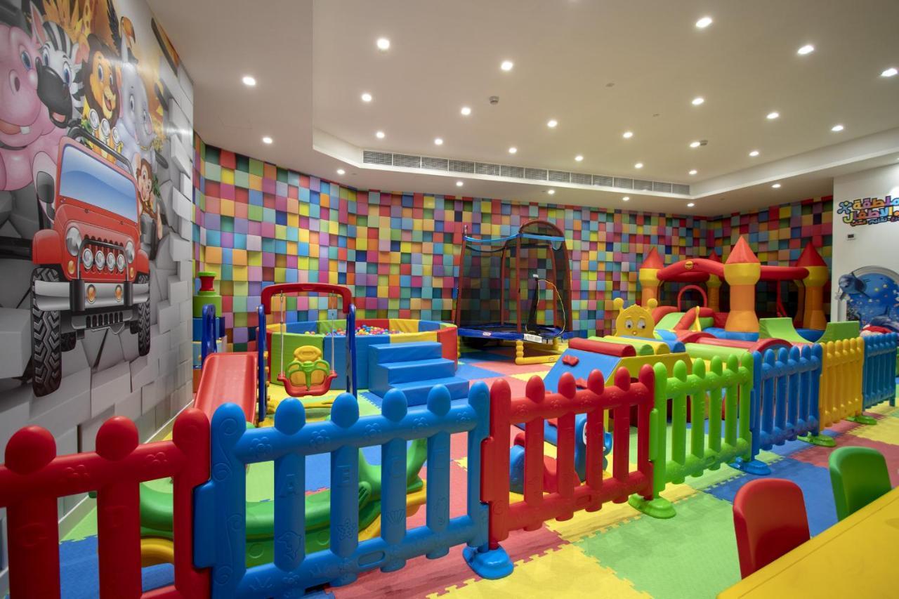 Wyndham Grand Manama Hotel Exterior photo The photo shows a colorful indoor play area designed for children. The space features various play equipment, including soft slides, climbing structures, and trampolines, surrounded by bright, padded flooring. There's a playful, multi-colored wall in